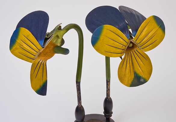 Ein Gipsmodell eine Stiefmütterchens in blau und gelb, aufgesteckt auf einem schwarzen Standfuß aus Holz