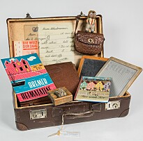 brauner Koffer, geöffnet, darin Lesefibel, Schiefertafel und ähnliches